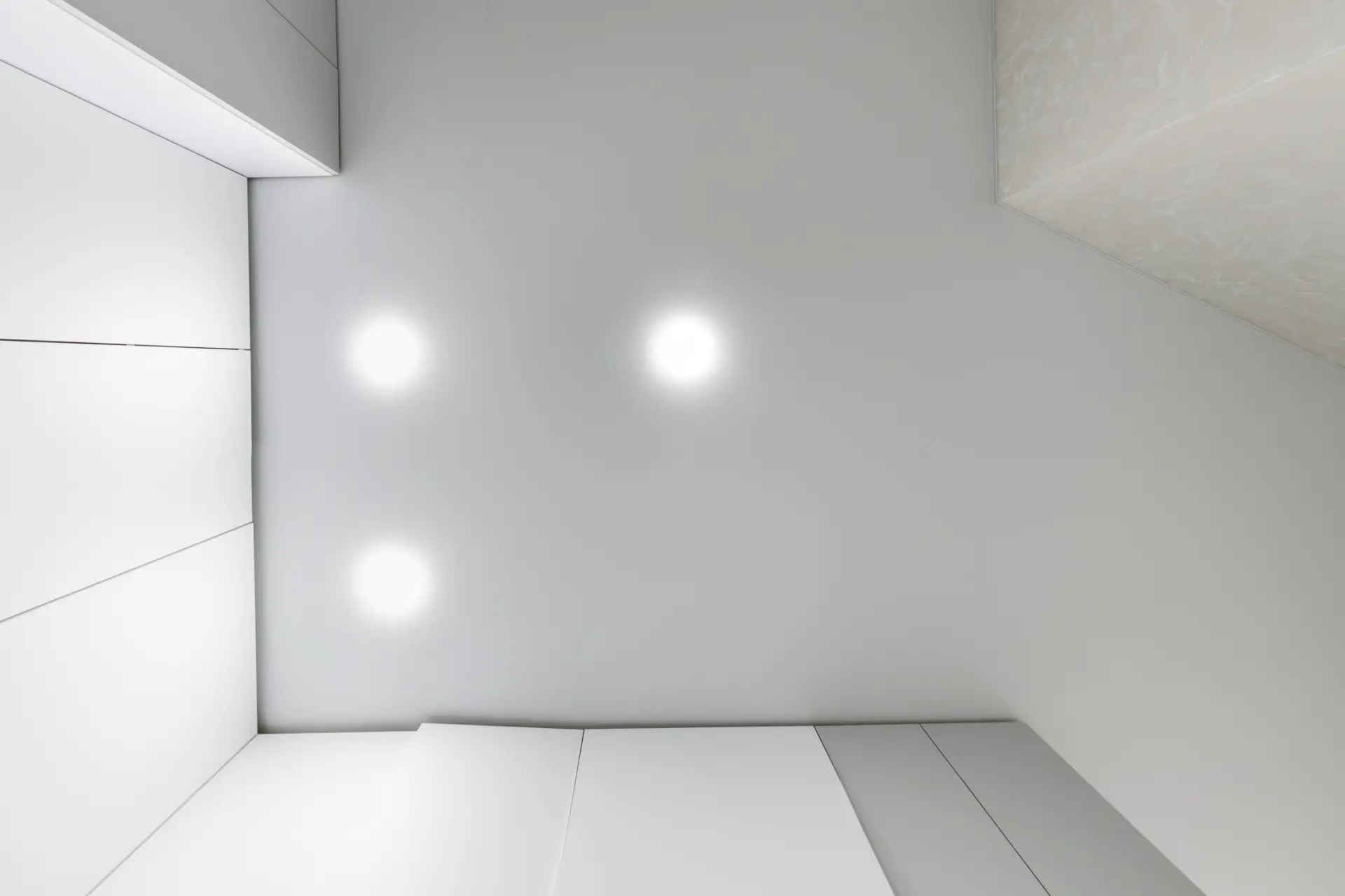 Hotový lesklý napínaný strop so zapustenými bodovými svetlami v minimalistickej miestnosti s moderným dizajnom.