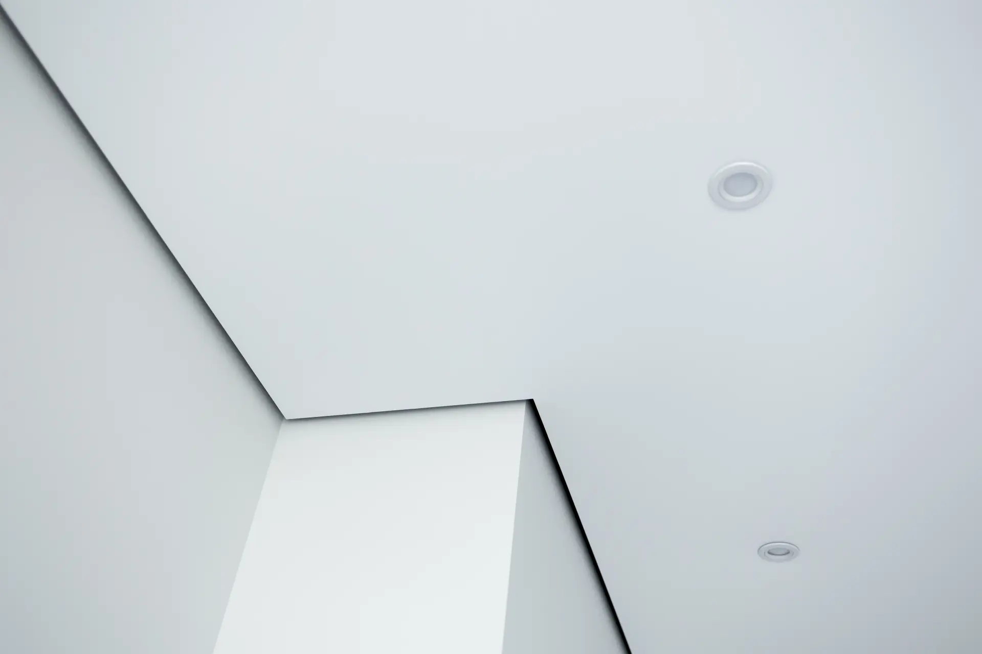 Minimalistický biely napínací strop s kruhovými zapustenými LED svietidlami v rohu miestnosti.